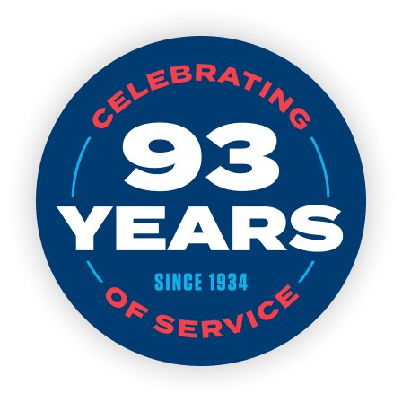 Blue circular anniversary badge reading 'Celebrating 93 Years of Service' with 'Since 1934' text