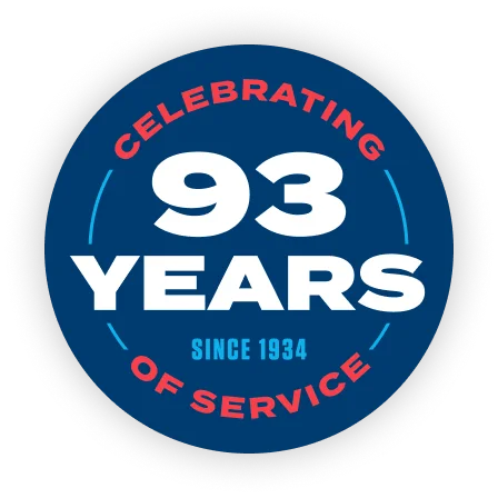 Blue circular anniversary badge reading 'Celebrating 93 Years of Service' with 'Since 1934' text