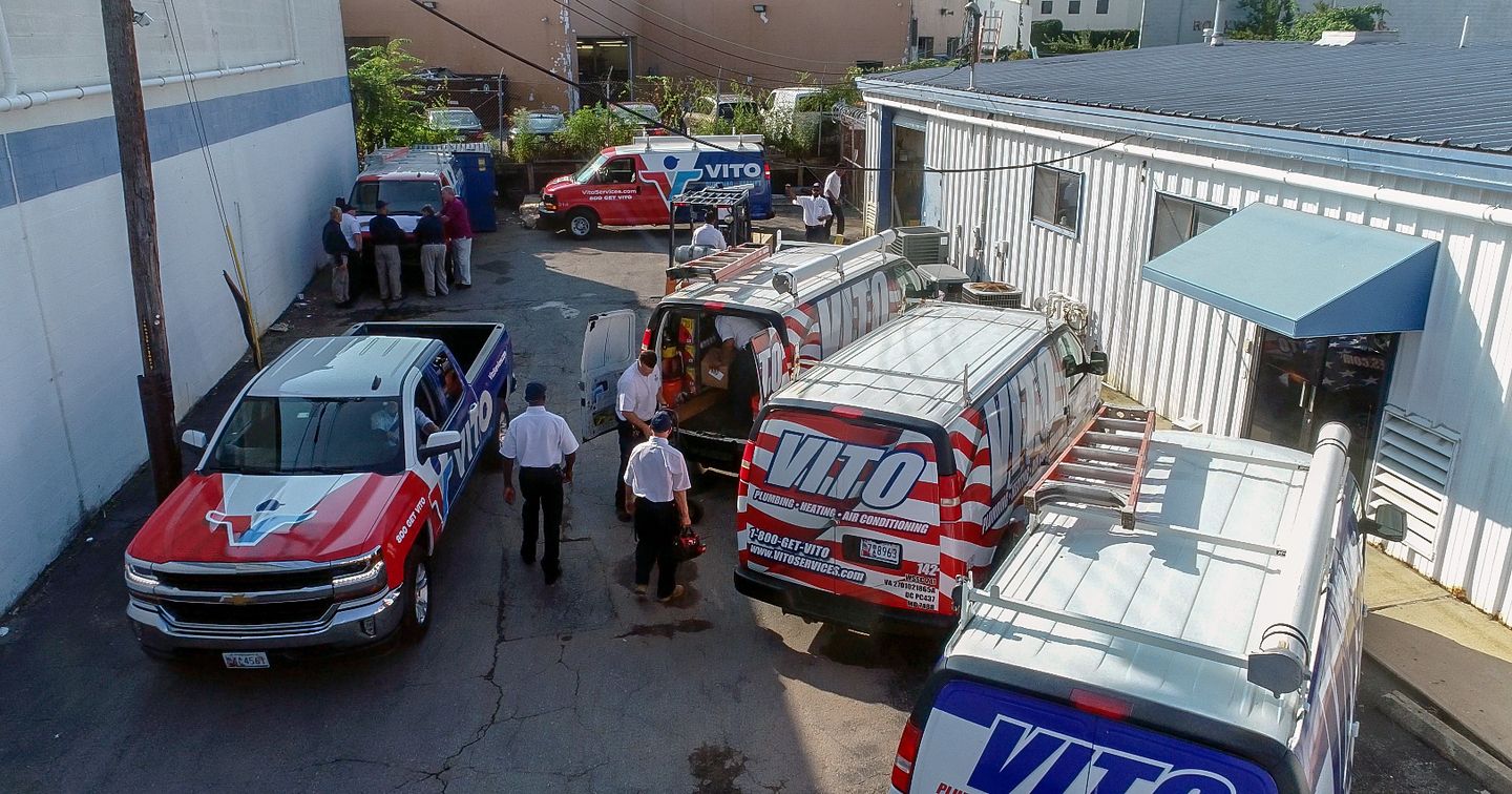 Row of VITO service vans and technicians in a narrow alley outside a building, preparing for repairs as a crew chats nearby.