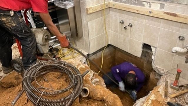 Plumbers underneath floor conducting sewer line repair.